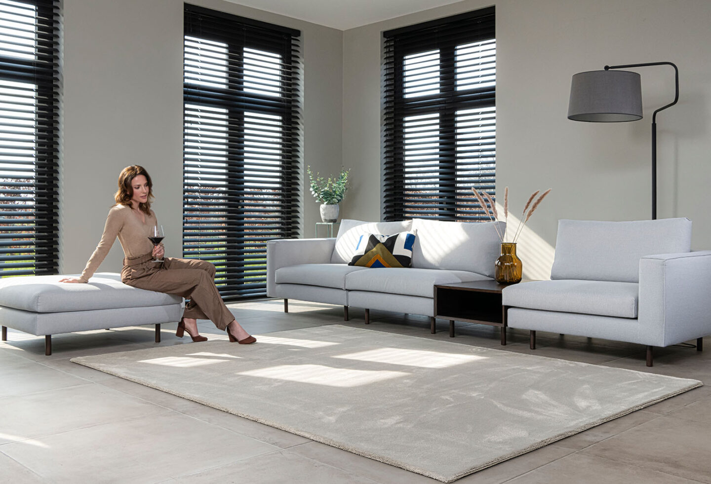 vrouw zit in woonkamer met groot zandkleurig vierkant vloerkleed op maat gemaakt